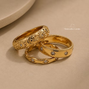 Peut inclure: Trois bagues dor&eacute;es orn&eacute;es de motifs c&eacute;lestes. Une bague pr&eacute;sente des gravures de soleil et de lune avec une pierre centrale, une autre a un bord textur&eacute; en corde avec des pierres en &eacute;toile, et la troisi&egrave;me est un anneau ondul&eacute; avec des pierres en &eacute;toile. Texte : Minimalist Lumin.