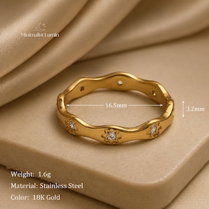 Peut inclure: Une bague en acier inoxydable dor&eacute; au design ondul&eacute;, orn&eacute;e de pierres transparentes serties en forme d'&eacute;toile. La bague a un diam&egrave;tre de 16,5 mm et une largeur de 3,2 mm. Le texte Minimalist Lumin est visible, ainsi que le poids de 1,6 g.