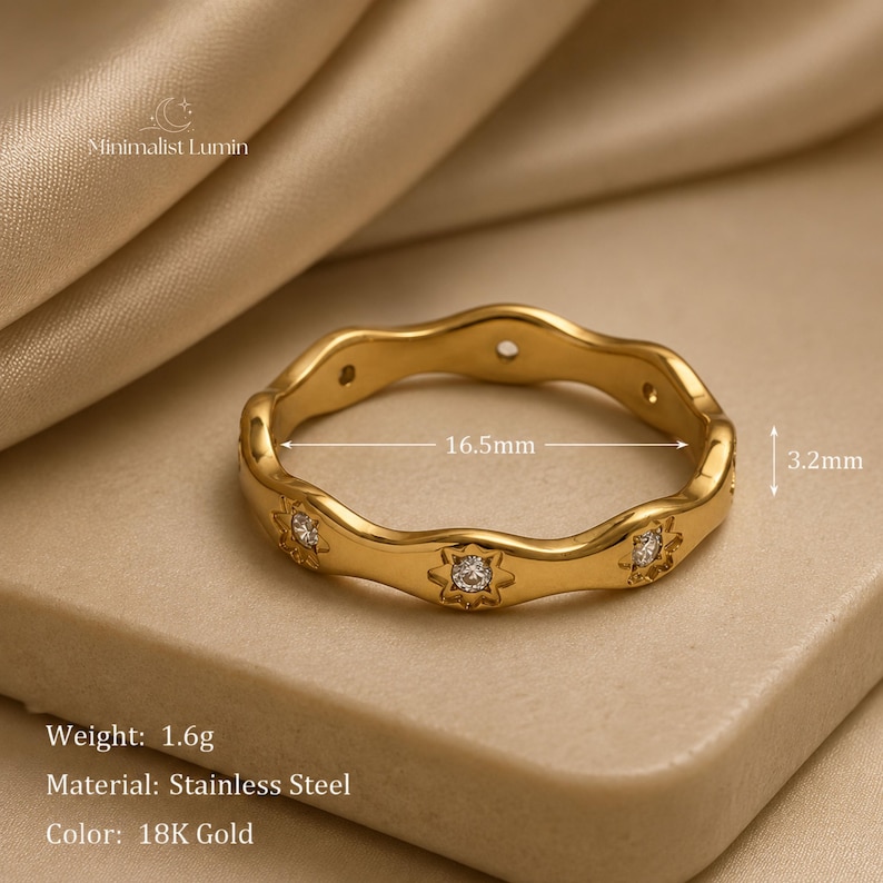 Peut inclure: Une bague en acier inoxydable dor&eacute; au design ondul&eacute;, orn&eacute;e de pierres transparentes serties en forme d'&eacute;toile. La bague a un diam&egrave;tre de 16,5 mm et une largeur de 3,2 mm. Le texte Minimalist Lumin est visible, ainsi que le poids de 1,6 g.