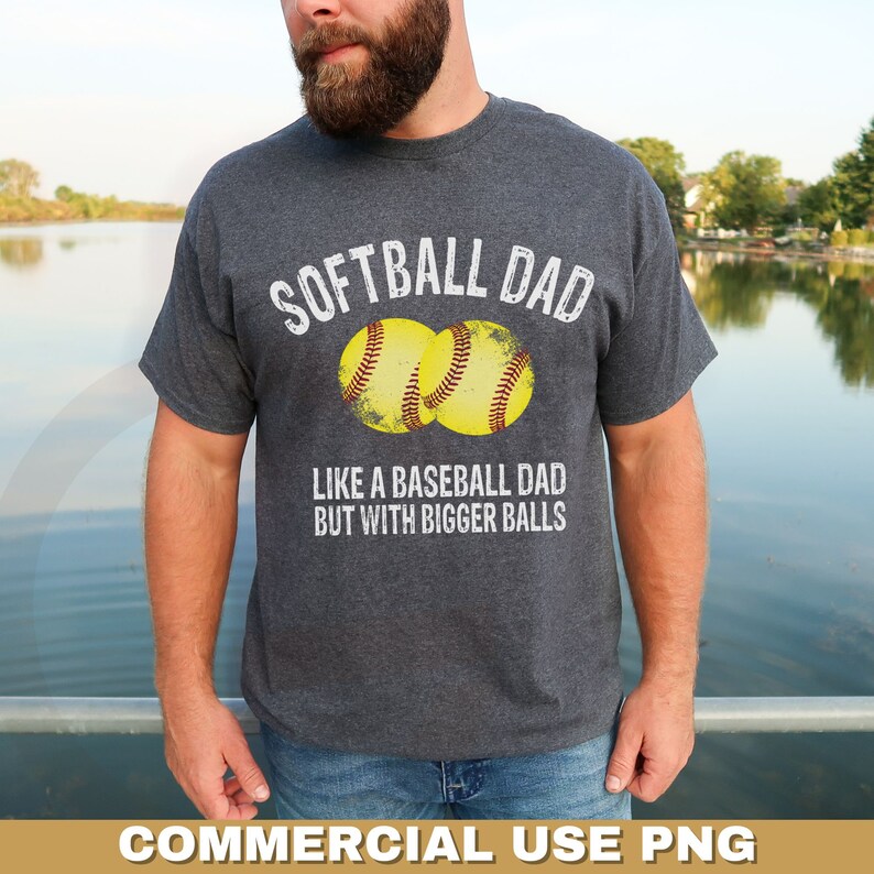Może przedstawiać: Szara koszulka z nadrukiem "Softball Dad" i dwoma ż&oacute;łtymi grafikami piłek do softballa. Tekst pod grafikami brzmi: "Jak tata baseballowy, ale z większymi piłkami."