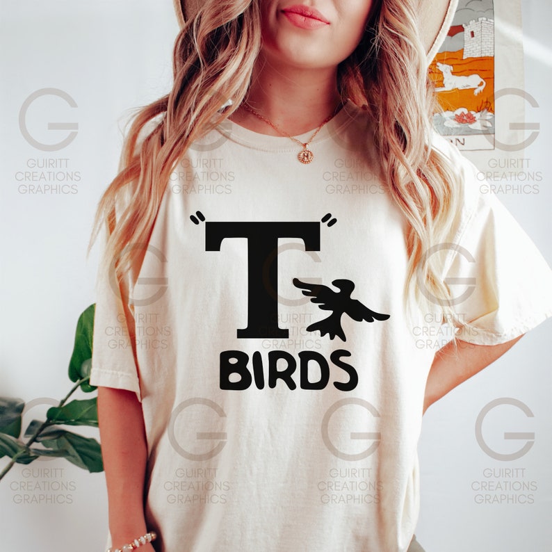 May include: A white t-shirt with a black graphic of a bird flying next to a large black letter "T" and the text "BIRDS" underneath.