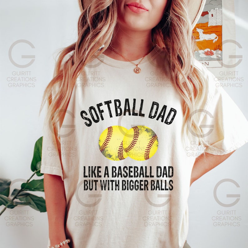 Może przedstawiać: Biała koszulka z napisem "Softball Dad Like a Baseball Dad But With Bigger Balls" w kolorze czarnym. Nad tekstem znajdują się dwie ż&oacute;łte grafiki przedstawiające piłki do softballa.