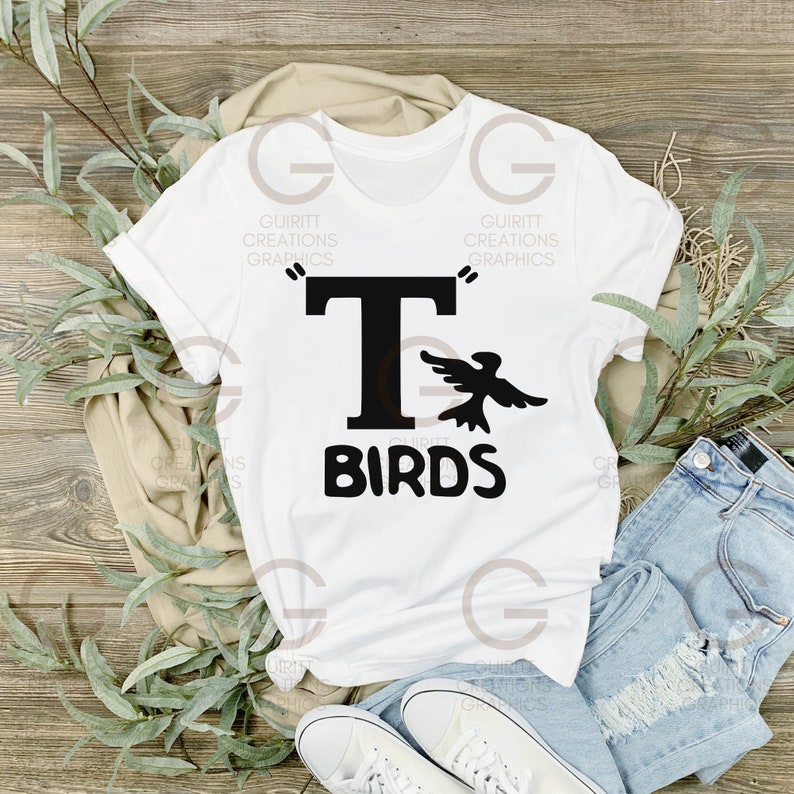 May include: White t-shirt with a black graphic of a bird flying next to a capital letter "T" and the text "BIRDS" underneath.