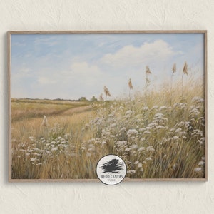 May include: A framed landscape painting shows a field of tall grasses and wildflowers under a blue sky with clouds. The artwork has a soft, painterly style, with warm, earthy tones. The frame is a light wood colour.