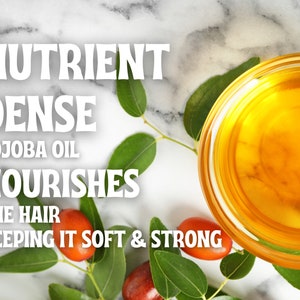 May include: A clear glass bowl filled with golden jojoba oil, surrounded by green leaves and red berries. The text "Nutrient Dense Jojoba Oil Nourishes The Hair Keeping It Soft & Strong" is displayed above the bowl.