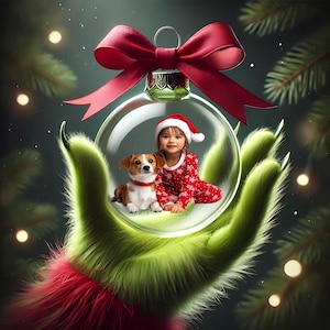 May include: A green, furry hand holds a clear glass ornament with a red bow. Inside the ornament, a young girl in a red and white holiday outfit sits with a small brown and white dog.