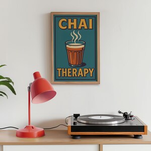 May include: A framed poster with the words "CHAI THERAPY" and an illustration of a chai tea cup. A red desk lamp and a record player are on a wooden surface.