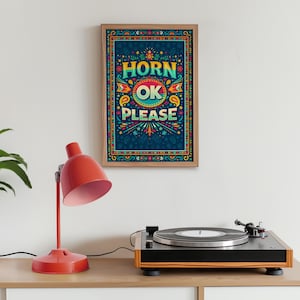 Pode incluir: Uma impressão artística emoldurada com as palavras "HORN OK PLEASE" em letras coloridas. A obra de arte tem um fundo azul-petróleo com desenhos florais e paisley. Uma lâmpada de mesa vermelha e uma vitrola estão em primeiro plano.