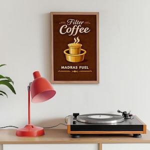May include: A framed poster with the words "Filter Coffee" and an illustration of a coffee filter. The poster is brown with gold lettering and a gold coffee filter illustration. A red desk lamp and a record player are in the foreground.