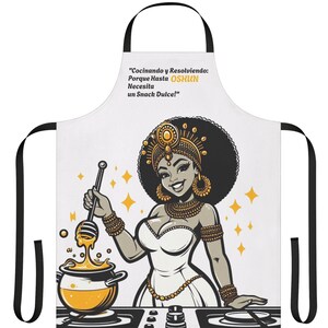 Könnte beinhalten: Eine weiße Schürze mit schwarzem Rand und einer bunten Illustration einer Frau beim Kochen. Der Text auf der Schürze lautet "Cocinando y Resolviendo: Porque Hasta OSHUN Necesita un Snack Dulce!"