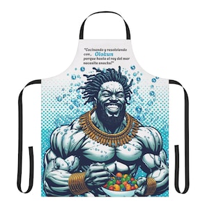 May include: White apron featuring a muscular, smiling figure with dreadlocks, wearing gold jewelry, and holding a bowl of colorful fruit. The apron has black straps and includes the text: "Cocinando y resolviendo con, Olokun porque hasta el rey del mar necesita snacks!"