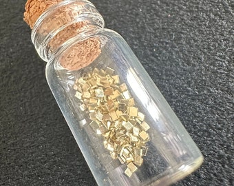 以下が含まれることがあります： コルク栓の付いた小さなガラス瓶に、金色のグリッターが入っています。