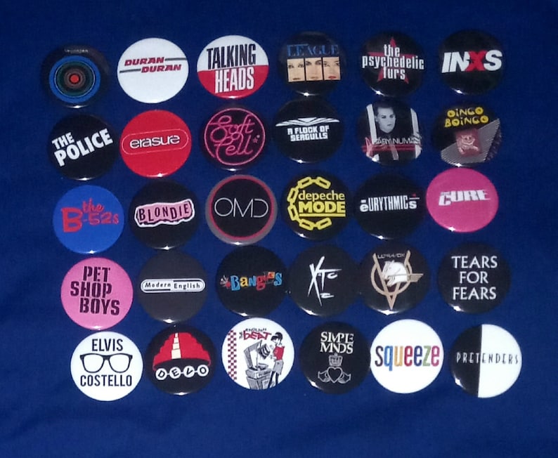 May include: A collection of 25 round buttons featuring various 80s music artists, including The Police, Duran Duran, Talking Heads, Blondie, and Tears for Fears. The buttons are colourful and feature band names and logos.