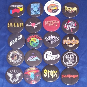 May include: A collection of 16 round button badges featuring various band logos, including Foreigner, Moody Blues, America, Nazareth, Supertramp, Fleetwood Mac, The Guess Who, Bad Company, Traffic, Dire Straits, Poco, Bachman Turner Overdrive, Asia, Chicago, Boston, Styx, and Badfinger.