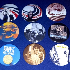 Puede incluir: Nueve botones redondos con varias imágenes del músico Elliott Smith. Los botones muestran portadas de álbumes, retratos y otras obras de arte relacionadas con su música. Todos los botones son en blanco y negro, excepto uno que es azul con una luna dorada.
