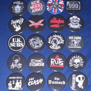 Op de afbeelding: Een verzameling van 16 zwart-witte punkrockband-knoppen. De knoppen bevatten bandnamen en logo's, waaronder The Clash, The Damned, The Stranglers, The Pogues en 999.