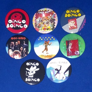 Puede incluir: Una colección de nueve botones redondos de la banda Oingo Boingo. Los botones presentan varios diseños, incluyendo el logotipo de la banda, imágenes de calaveras y arte de álbumes. Los colores incluyen rojo, negro, azul y verde.