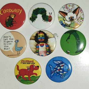 May include: A collection of eight circular pin-back buttons featuring illustrations from children's books, including Corduroy, The Very Hungry Caterpillar, a Siamese cat, Don't Let the Pigeon Drive the Bus, a rainbow-colored child, The Giving Tree, Clifford the Big Red Dog, and a Rainbow Fish.