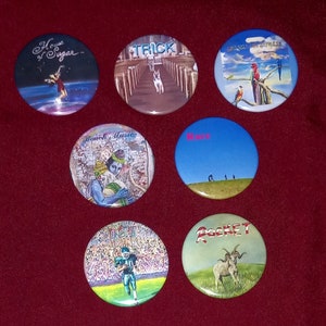May include: Seven round buttons with different album covers. The buttons are on a red surface. The album covers include "House of Sugar", "Trick", "Get Your Wings", "Beach Music", "Rare", "Pocket", and "Freebird".