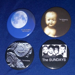 Op de afbeelding: Vier ronde zwart-witte knoppen met de bandnaam "The Sundays" erop gedrukt. De knoppen tonen verschillende afbeeldingen: een volle maan, een babygezicht, een cirkelpatroon en een bandfoto.
