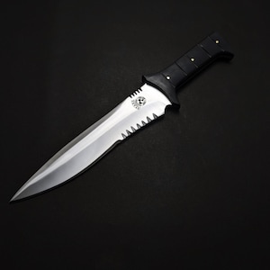May include: A silver and black knife with a serrated edge and a pointed tip. The handle is black with gold-colored rivets. The knife has a decorative emblem near the blade's base. The background is black.
