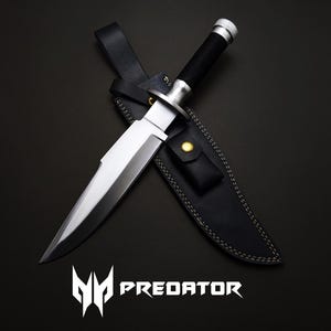 Könnte beinhalten: Ein großes Messer mit silberner Klinge, schwarzem Griff und schwarzer Lederscheide. Das Messer hat einen silbernen Handschutz und Knauf. Die Scheide hat einen Druckknopfverschluss. Das Wort "PREDATOR" wird darunter angezeigt.