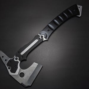 May include: A tactical hatchet featuring a matte black curved handle with textured grip sections and a silver metal inlay. The head is constructed from dark grey metal, showcasing a sharp blade edge, a pointed spike, and a circular cutout.