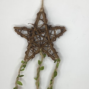 May include: A brown twig star with three strands of twine hanging from it. Each strand has green leaves and a cluster of gold bells.