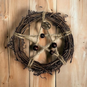 May include: A brown twig wreath with a pentagram woven into it. The pentagram is made of twine and has five brown beads at each point. A gold star charm hangs from the top of the pentagram.