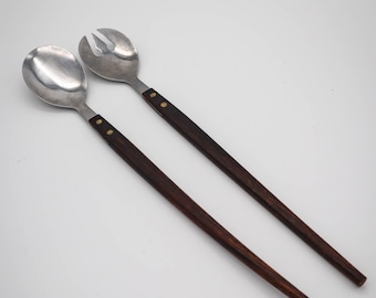 May include: A set of two salad servers with wooden handles. The handles are dark brown with gold accents. The metal parts are silver.