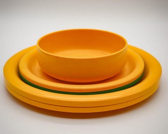 May include: A set of three yellow plastic bowls with a green rim. The bowls are stacked on top of each other.