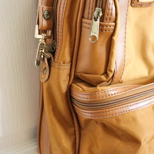 Pu&ograve; includere: Primo piano di una borsa da viaggio marrone e beige. La borsa presenta una combinazione di tessuto beige e dettagli in pelle marrone. Ha pi&ugrave; cerniere, elementi metallici e un design strutturato. La borsa sembra ben fatta e resistente.