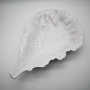 May include: A white ceramic leaf-shaped serving dish. The dish has a glossy finish and detailed veining, mimicking a real leaf. The edges are gently scalloped, adding to the naturalistic design. Ideal for serving appetizers or as a decorative piece.