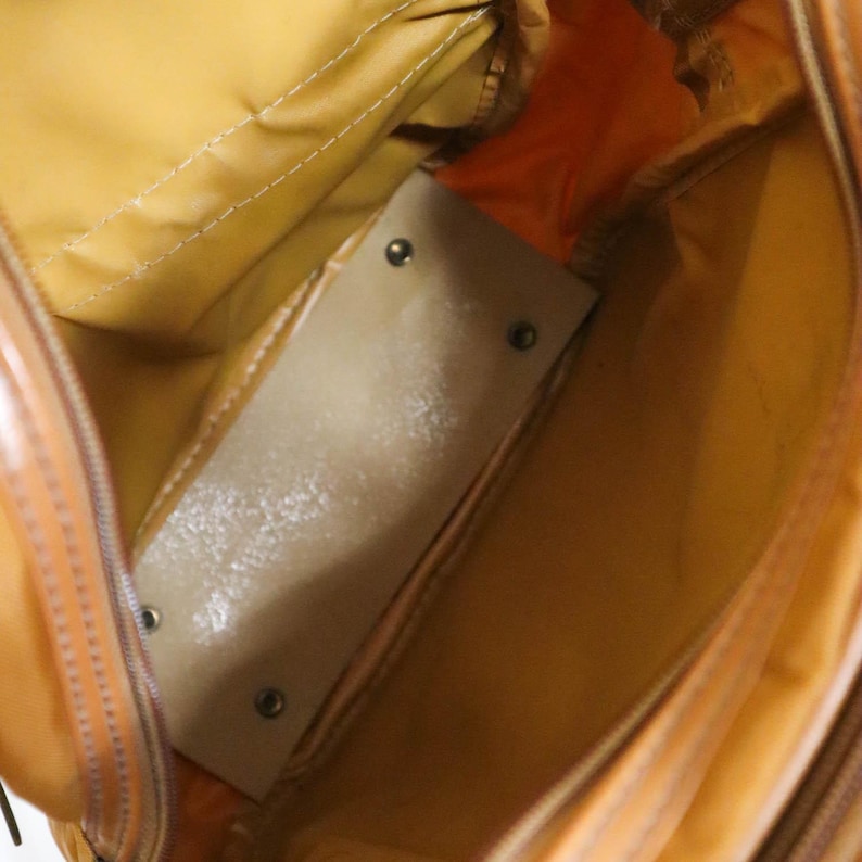 Pu&ograve; includere: Vista interna di una borsa beige e arancione. L'interno della borsa &egrave; di colore beige chiaro, con un divisore rettangolare di colore chiaro fissato con rivetti. L'esterno della borsa &egrave; arancione lucido, con cuciture visibili e una cerniera.