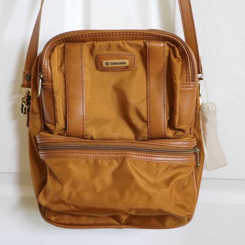 Pu&ograve; includere: Borsa a tracolla Samsonite color marrone dorato. La borsa ha una forma rettangolare con uno scomparto principale con cerniera e una tasca frontale pi&ugrave; piccola. Presenta dettagli in pelle marrone e una tracolla. Il logo Samsonite &egrave; visibile.