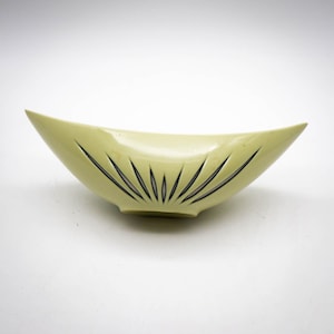May include: A pale yellow ceramic bowl with a black and white sunburst design. The bowl is shaped like a boat and has a rounded bottom.