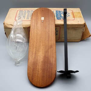 May include: A vintage wooden barometer with a clear glass weather forecasting instrument and a black metal candle holder. The barometer has a light brown wooden backboard and is accompanied by a cardboard box.