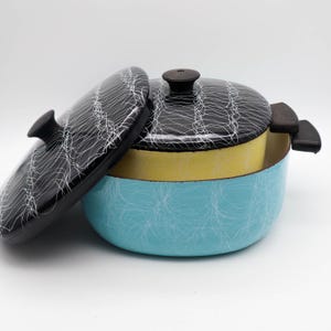 May include: A vintage enamelware cooking pot with a lid. The pot is light blue with a white web-like pattern. The interior is yellow. The lid and handles are black with a white web-like pattern. The lid has a black knob.