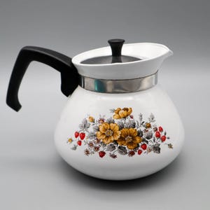 May include: White ceramic teapot with a black handle and lid. The teapot features a floral design with yellow flowers, red strawberries, and gray leaves. A silver band encircles the middle of the teapot.