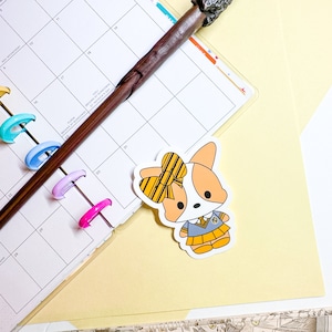 May include: A sticker of a cartoon corgi wearing a yellow and black striped bow, a blue and gray uniform, and a yellow badge. The corgi is standing on a yellow background.