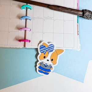 May include: A sticker of a cartoon dog wearing a blue and white striped bow, a grey and blue school uniform, and a blue skirt. The dog has a brown and white fur pattern.