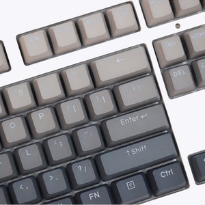 K&ouml;nnte beinhalten: Nahaufnahme einer mechanischen Tastatur mit grauen Tastenkappen. Die Tasten sind in einem Standard-Layout angeordnet, mit alphanumerischen Tasten, Funktionstasten und Pfeiltasten. Die Tastenkappen haben ein Farbverlauf, der von hellgrau zu dunkelgrau &uuml;bergeht.