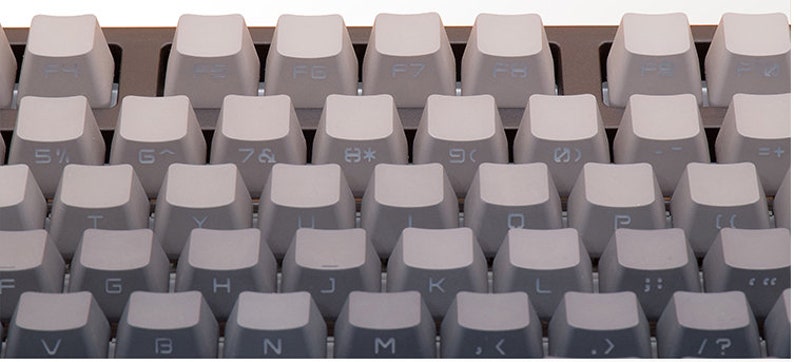 K&ouml;nnte beinhalten: Nahaufnahme einer Computertastatur mit hellgrauen Tastenkappen. Die Tasten sind in einem Rastermuster angeordnet, wobei verschiedene Symbole und Buchstaben sichtbar sind. Die Tastatur hat ein modernes, minimalistisches Design.