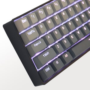 K&ouml;nnte beinhalten: Nahaufnahme einer schwarzen mechanischen Tastatur mit grauen Tastenkappen. Die Tasten sind mit einem violetten Licht hinterleuchtet. Die Tastatur hat ein Standard-QWERTZ-Layout mit Funktionstasten und Steuertasten.