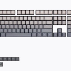 K&ouml;nnte beinhalten: Ein Satz Tastenkappen in verschiedenen Gr&ouml;&szlig;en und Layouts, f&uuml;r eine mechanische Tastatur. Die Tastenkappen sind &uuml;berwiegend grau mit einem Farbverlauf, der von dunkleren zu helleren Farbt&ouml;nen &uuml;bergeht. Das Set enth&auml;lt Tasten f&uuml;r den Haupttastaturbereich, den Ziffernblock und Funktionstasten.