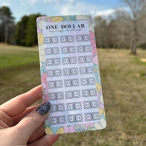 May include: A sheet of stickers with a floral design and the text "ONE DOLLAR savings challenge". The stickers feature 30 black and white dollar bill icons.