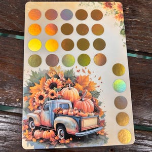 May include: A rectangular sticker sheet featuring a collection of circular holographic foil swatches in various metallic shades. The bottom section displays a colorful illustration of a vintage pickup truck loaded with pumpkins, sunflowers, and autumn leaves.