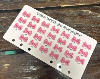 May include: A white savings tracker card with 26 pink bow illustrations, each with a dollar amount. The text "26 Bows to Watch Your Savings Grow!" is printed at the top. The card has three holes for binder use.