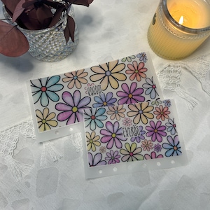 May include: Two clear plastic sheets with a repeating pattern of colorful daisies. The top sheet has the word "kahoot" written on it. The bottom sheet has the word "extras" written on it.