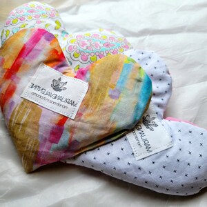 May include: Two heart-shaped fabric pillows with colorful abstract patterns and white labels. The labels have the text "ZITIVJAVBWALIAAN" and "VBVALIRAM" on them.